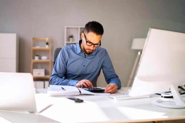 bufiscom-article-journal-recette-bureau Homme effectuant sa comptabilité à son bureau.