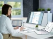 Une femme professionnelle utilisant un logiciel de facturation électronique sur plusieurs écrans dans un bureau moderne, illustrant le concept de digitalisation et de gestion des factures en ligne.