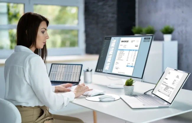 bufiscom-peppol-mercurius-facturation-electronique Une femme professionnelle utilisant un logiciel de facturation électronique sur plusieurs écrans dans un bureau moderne, illustrant le concept de digitalisation et de gestion des factures en ligne.